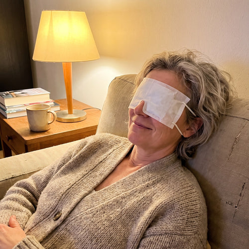 Frau entspannt am Abend mit Wärmemaske auf dem Sofa (Modell)